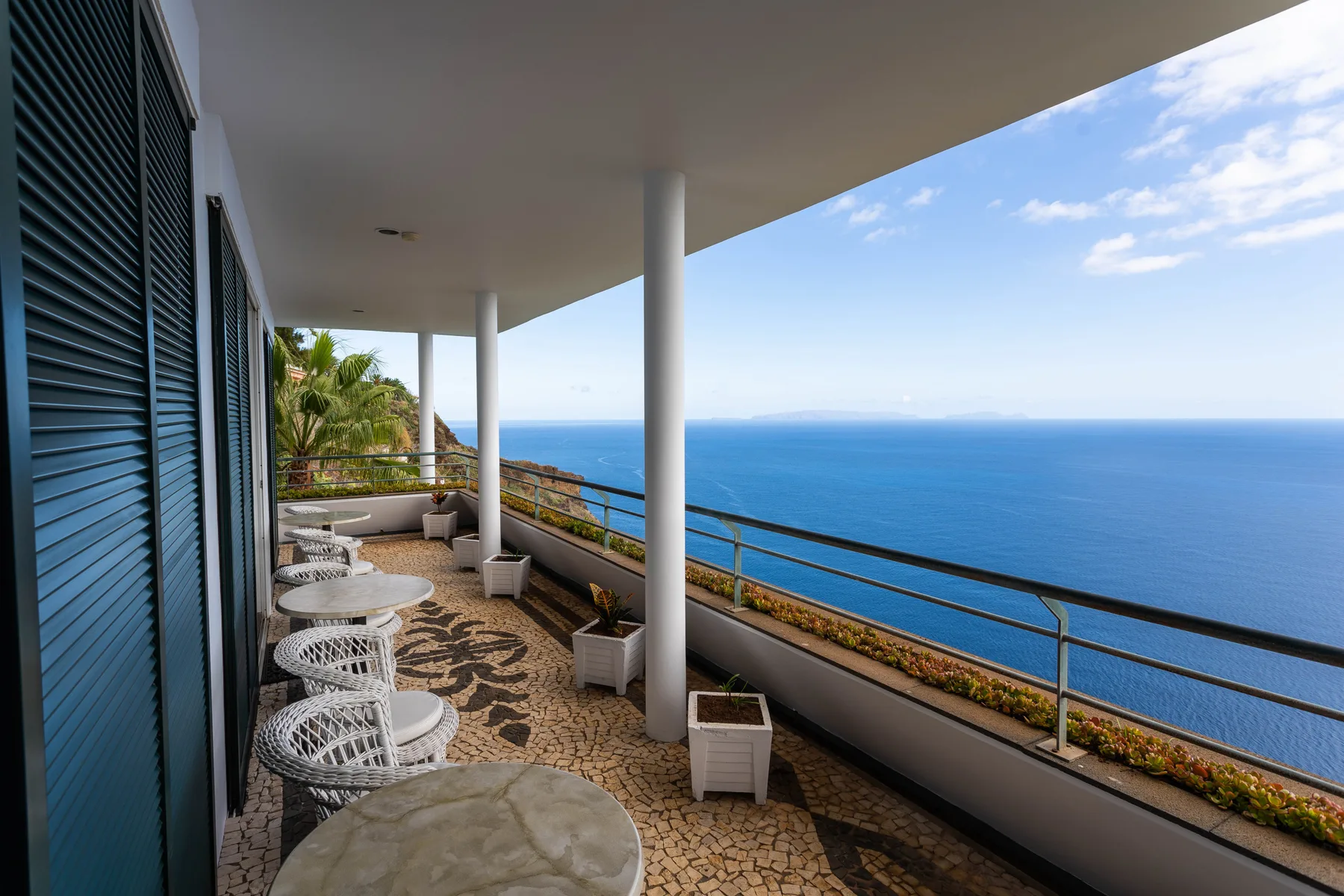 A covered terrace overlooks the sea, with seating and small tables along the railing.