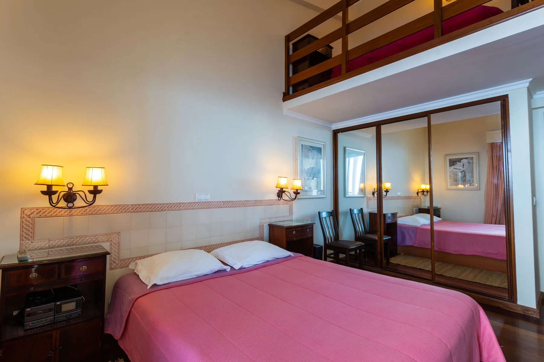 A bedroom with pink bedding and a raised sleeping area.