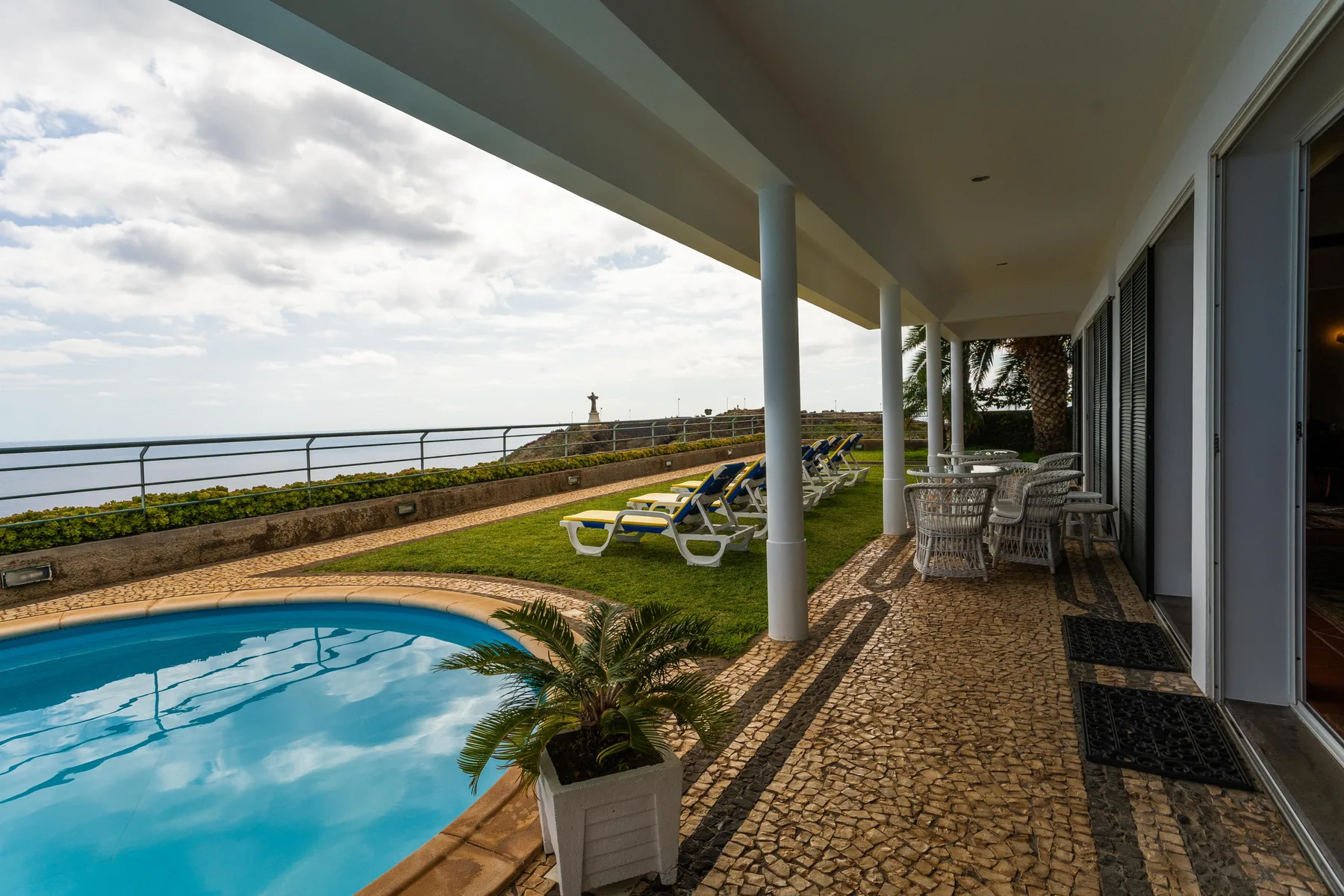 Un patio cubierto da a una piscina, un césped y el mar.