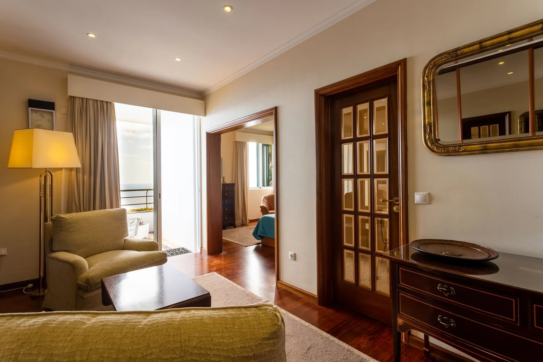 Una sala de estar con asientos, una lámpara de pie y una luminosa puerta al balcón.