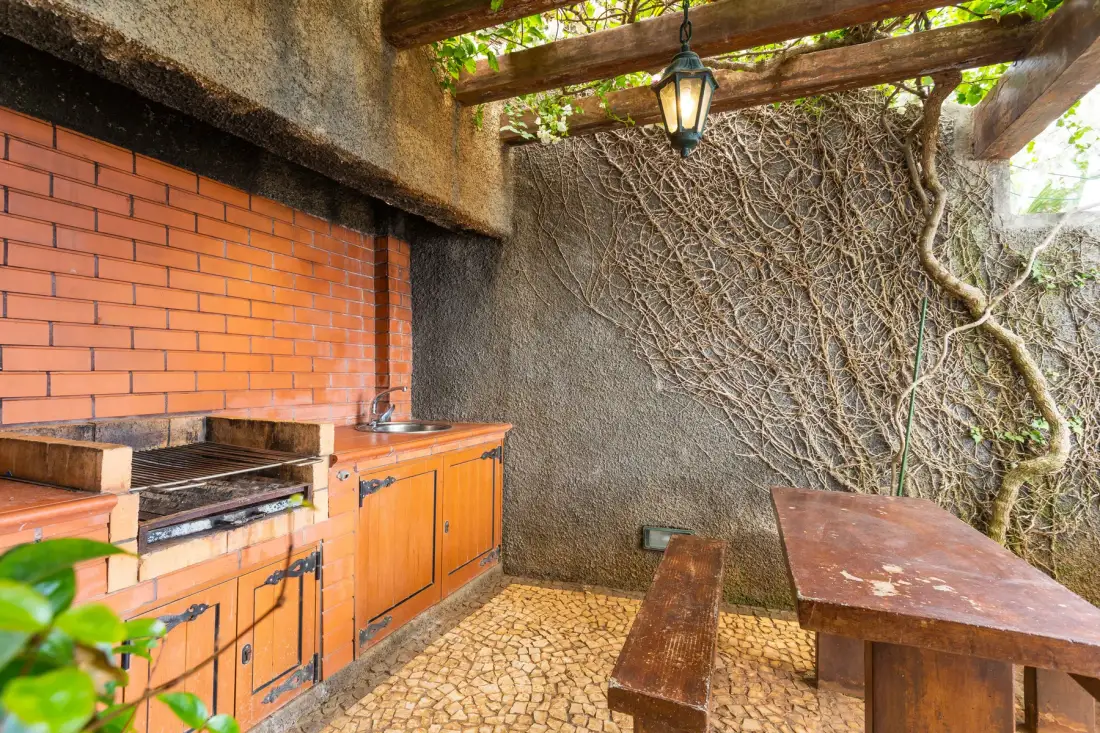 Un comedor al aire libre con una barbacoa de ladrillo y una mesa de madera bajo una pérgola.