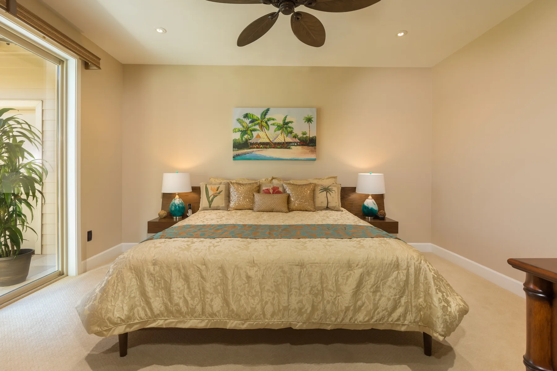 Un dormitorio con una cama grande bajo una pintura tropical y un ventilador de techo.