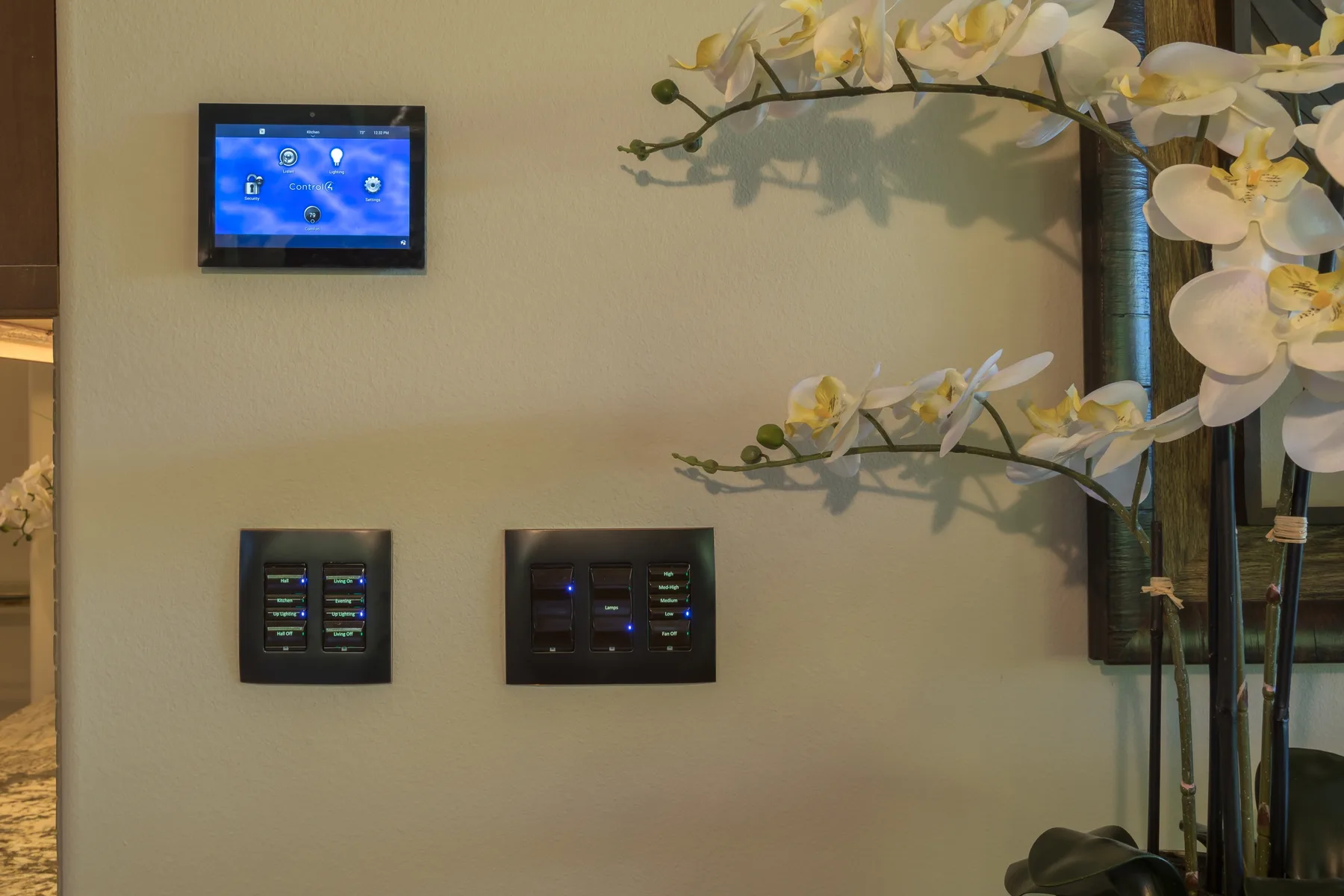 Un panel de control está montado en la pared junto a ramas decorativas de orquídeas.