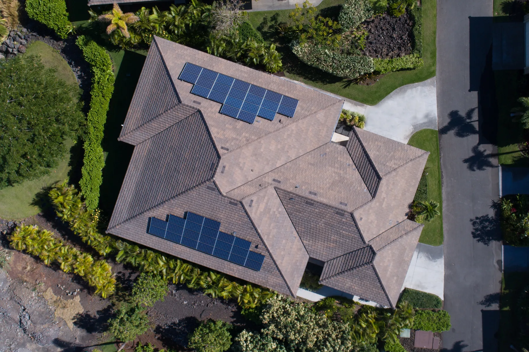 Vista aérea de una casa con paneles solares en el techo, rodeada de jardines.