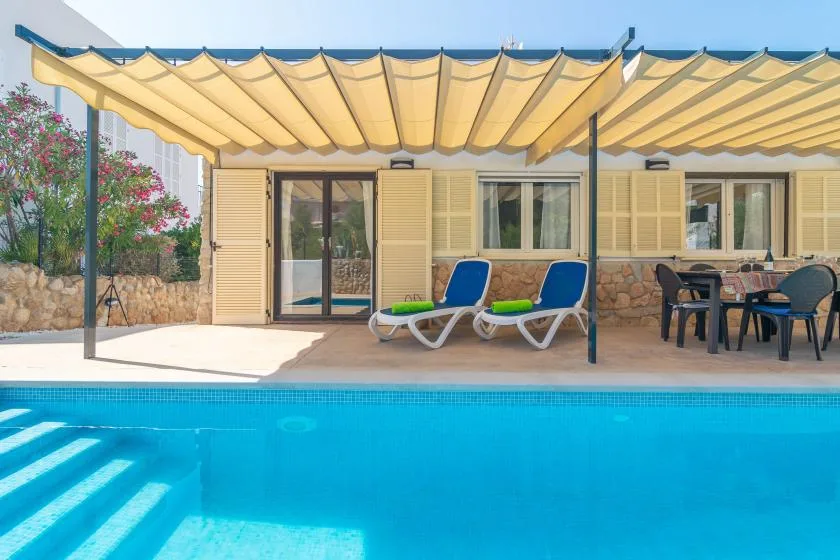 A swimming pool beside a house, with lounge seating and a shaded patio.