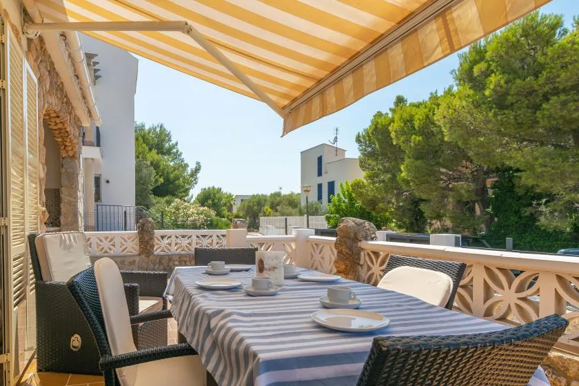 A shaded outdoor dining terrace with a long table and surrounding greenery.