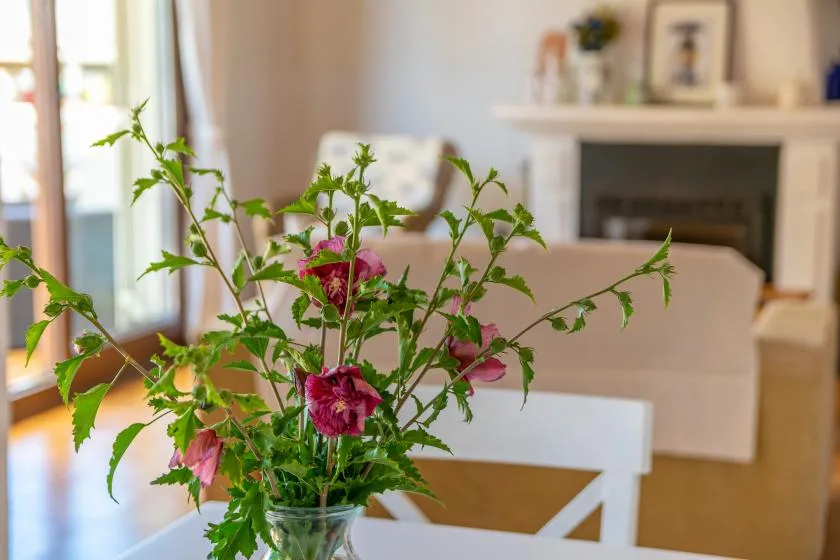 A living room with a vase of flowers in the foreground and a fireplace behind the seating.