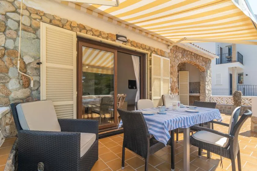 An outdoor dining terrace with a striped awning and stone walls.