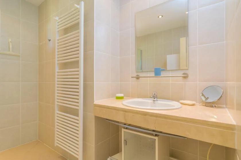 A tiled bathroom with a sink, mirror, and wall-mounted towel warmer.