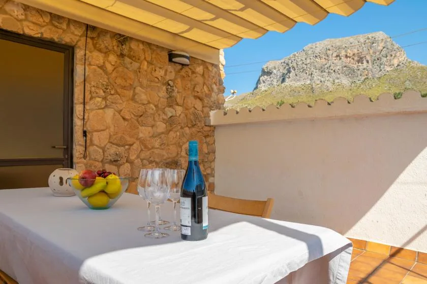 A covered outdoor dining area with a table set with fruit and wine glasses.