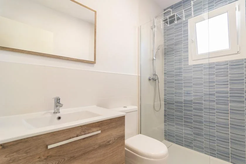 A bathroom with a vanity, toilet, and shower beside a tiled wall.