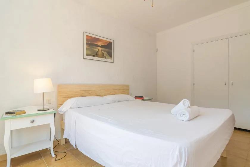 A bedroom with a neatly made bed, a bedside table, and a lamp.