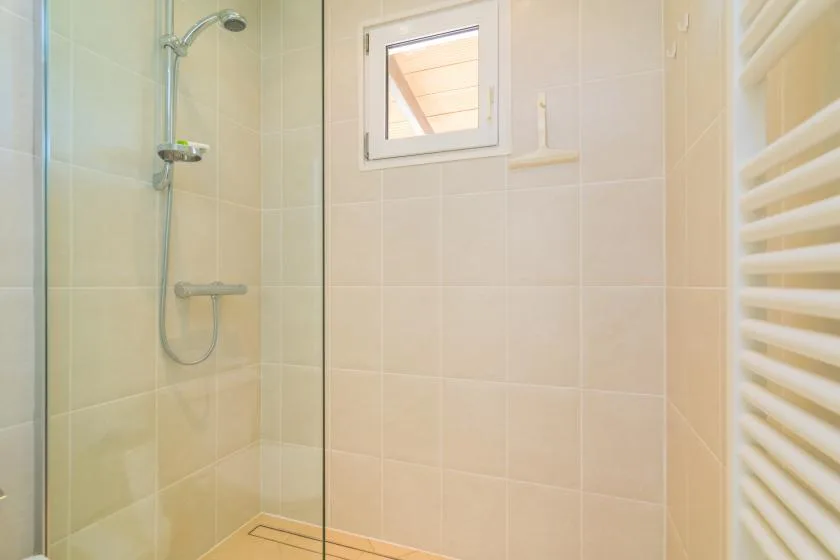 A tiled shower area with a small window and a wall-mounted towel radiator.