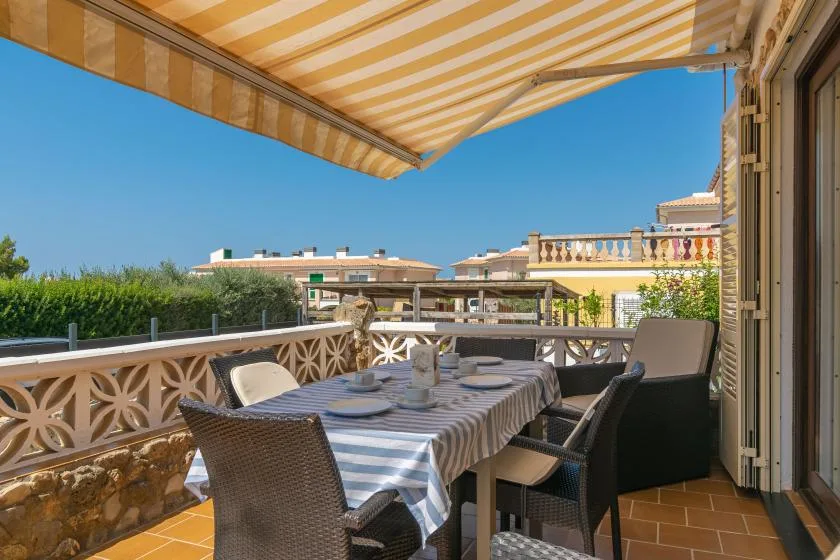 A sunny outdoor dining terrace with a table and seating under a striped awning.
