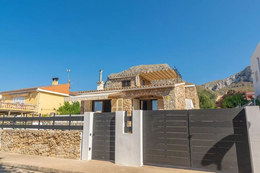 Stone house behind a dark front gate, with hills visible in the background.