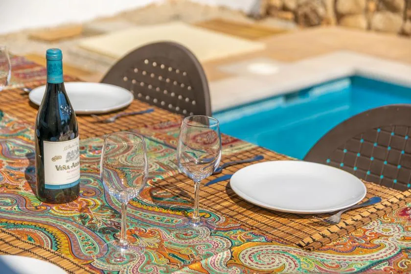 A dining table set with plates and glasses sits beside a swimming pool.