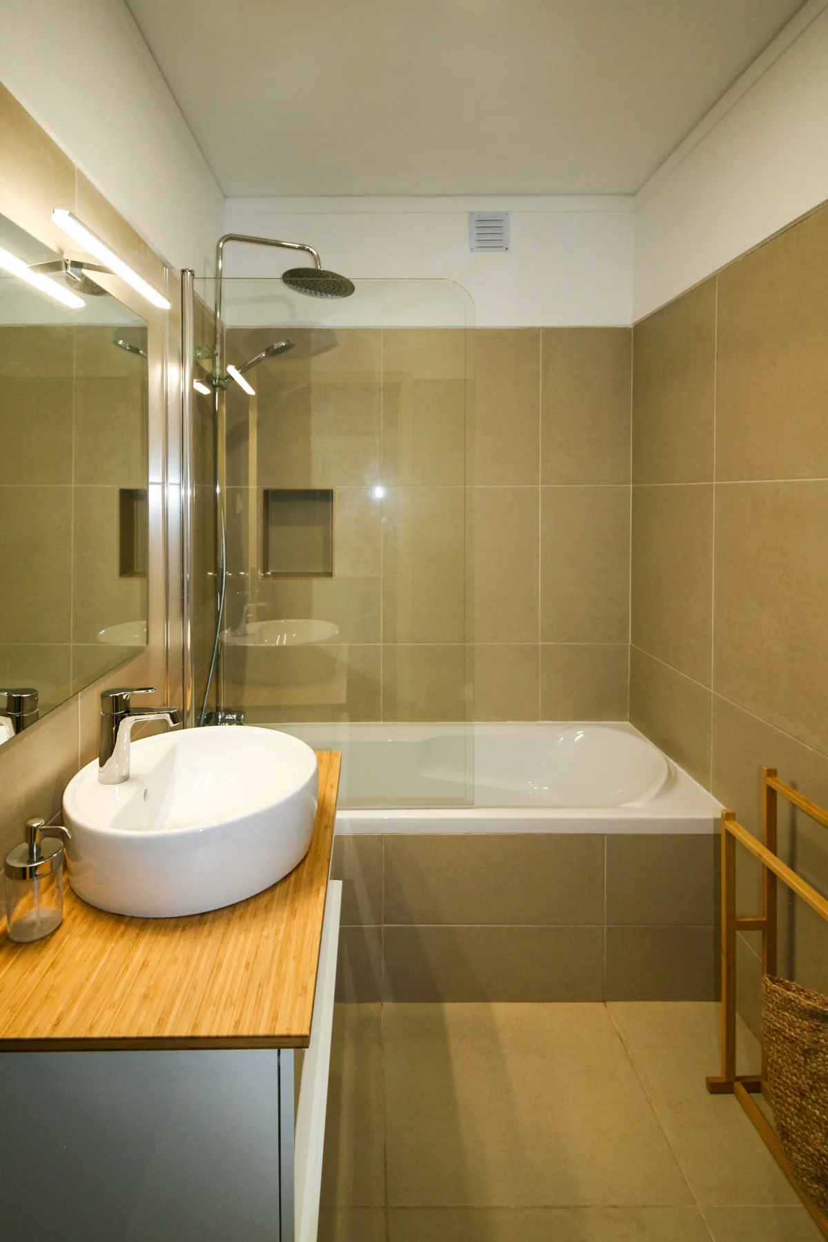 Un baño alicatado con bañera y lavabo sobre un mueble de madera.