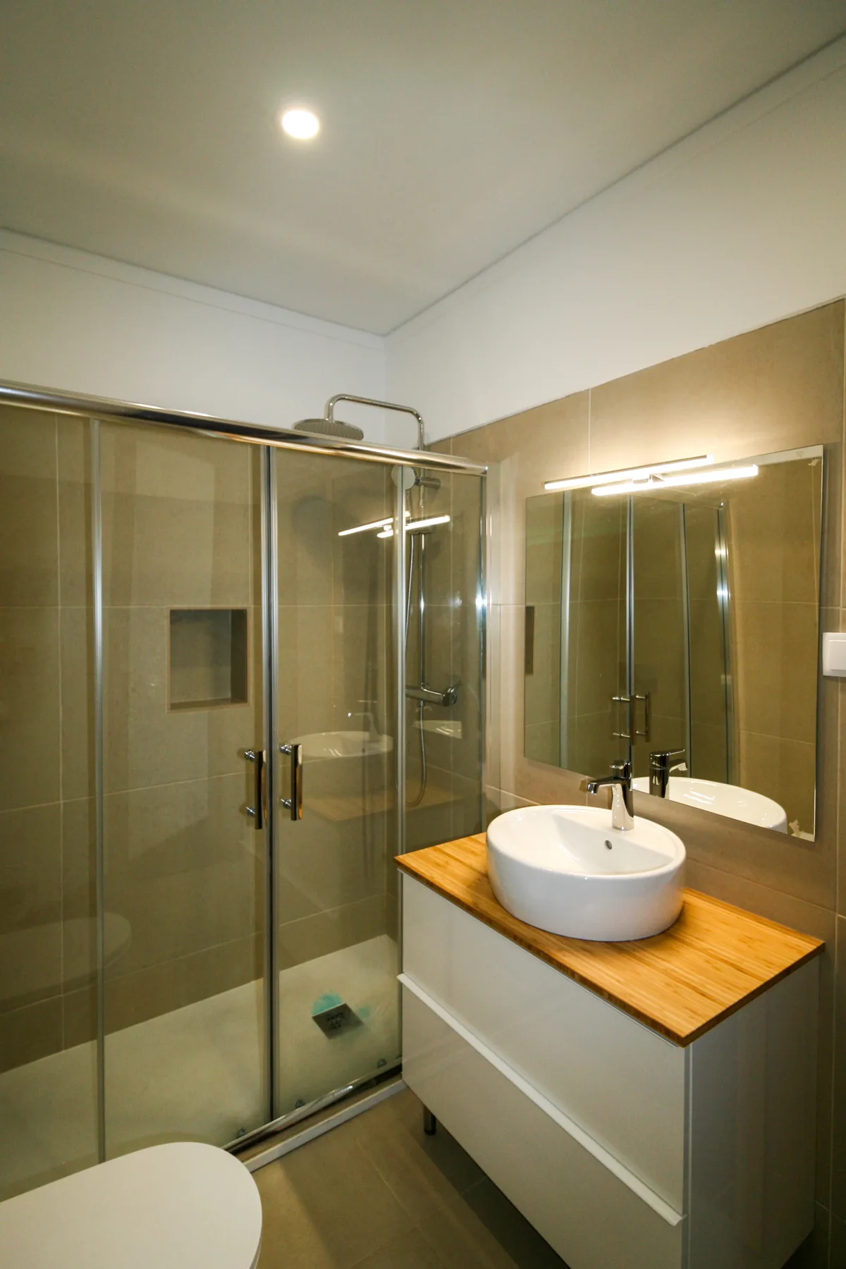 Un baño con azulejos, una ducha de vidrio y un lavabo bajo un espejo grande.