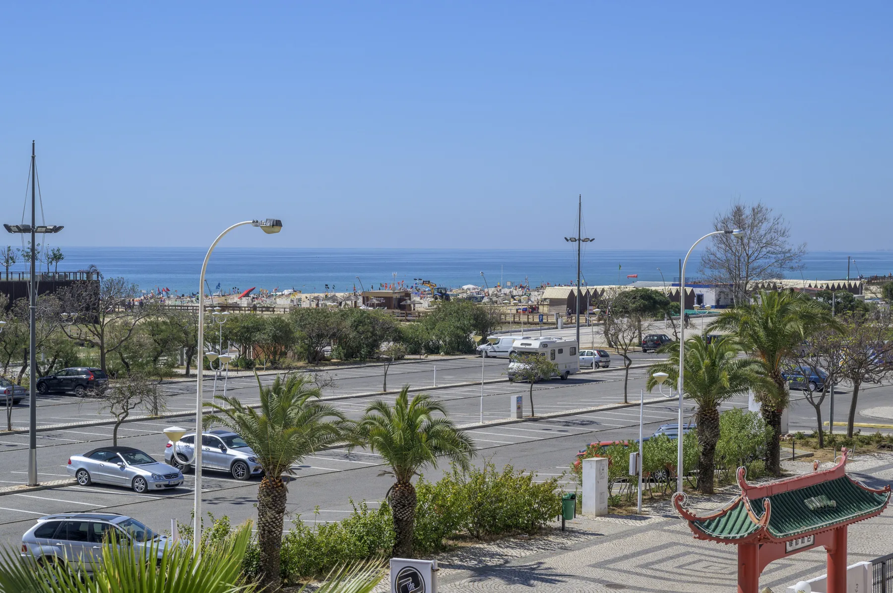 A coastal parking area with palm trees and the sea visible in the distance.