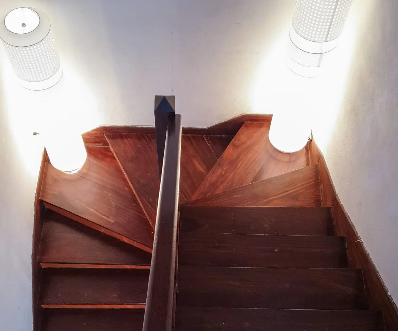 A wooden staircase turns between white walls beneath ceiling lights.