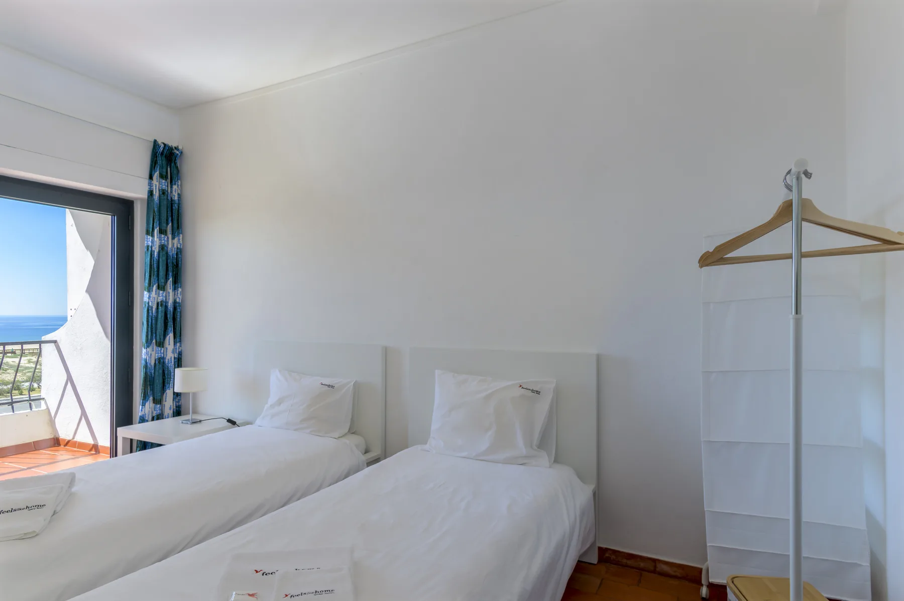 A bright bedroom with two single beds and a clothing rack.