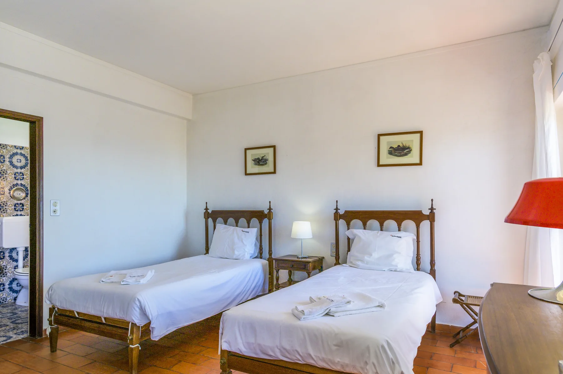 A bedroom with two beds, bedside tables, and framed pictures on the wall.