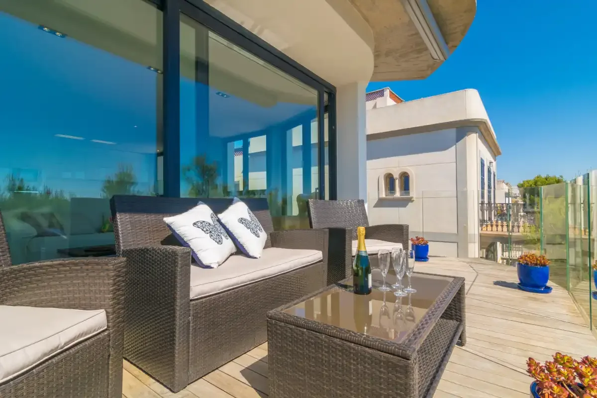 A furnished terrace beside large glass windows overlooks neighboring buildings.