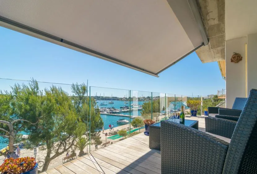 An outdoor terrace overlooks a marina, with dark woven seating beside a glass railing.
