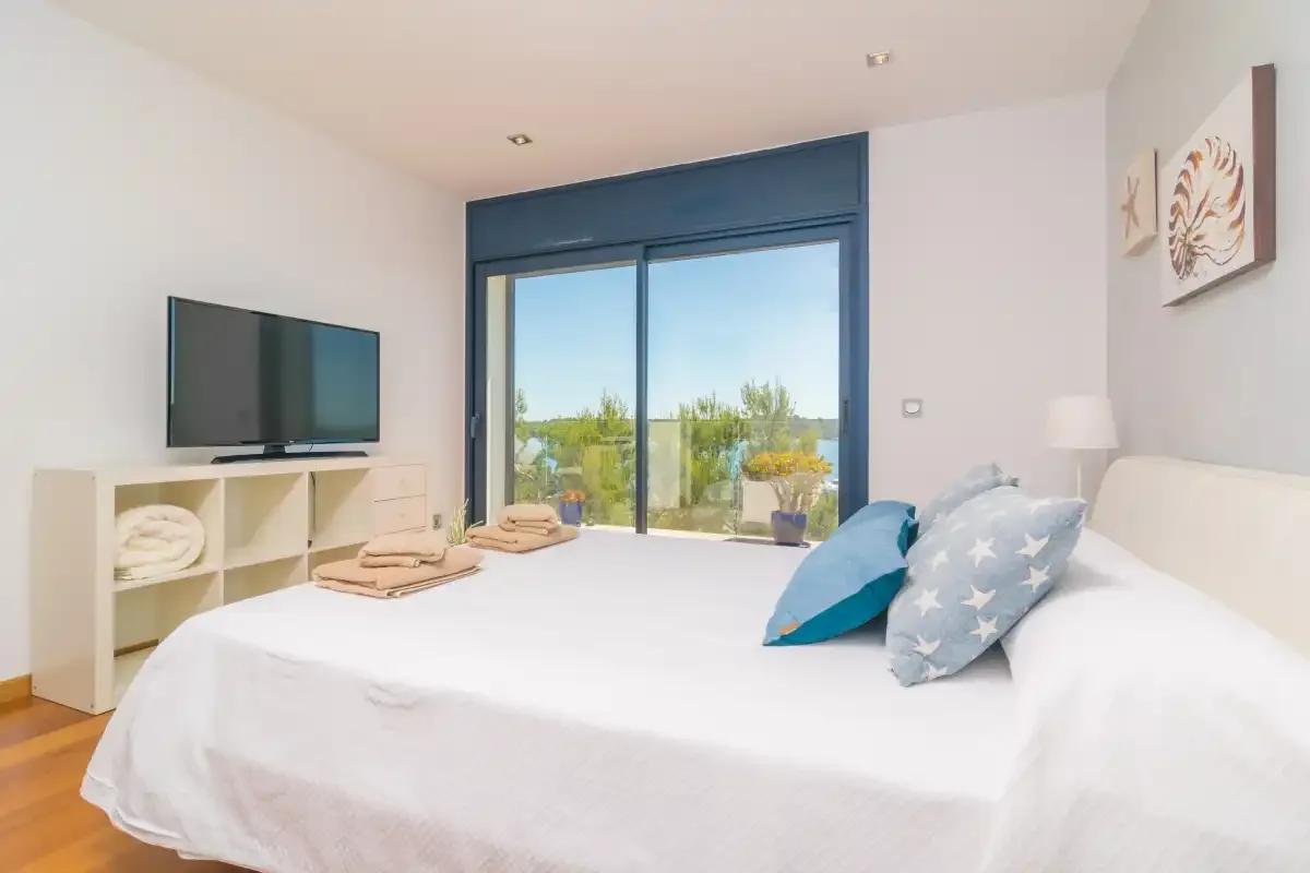 A bright bedroom with a bed, television, and sliding glass doors opening to a garden.