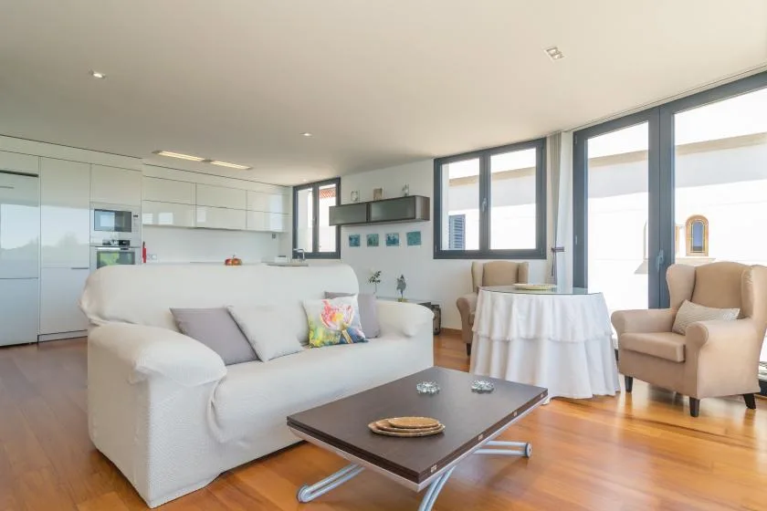 A bright living room with white seating, a coffee table, and large windows.
