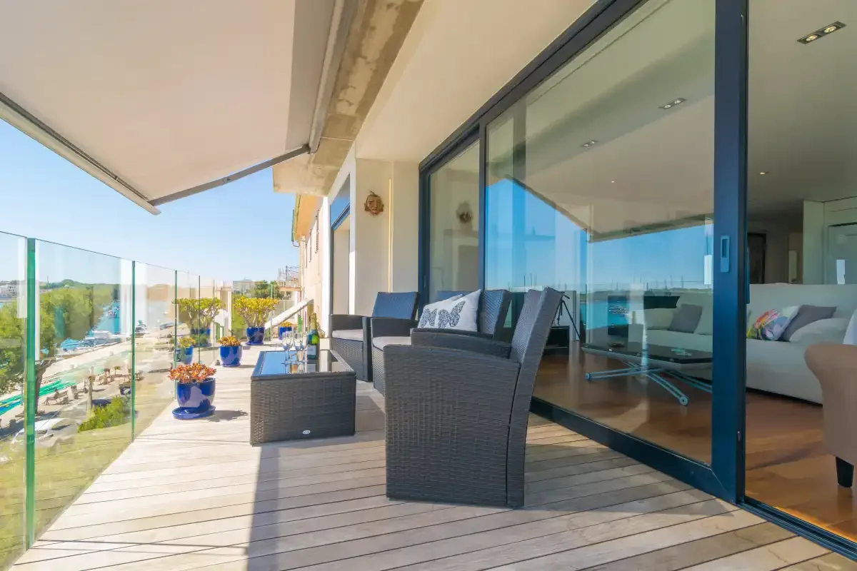 A furnished balcony with outdoor seating and glass doors opening onto an interior living area.