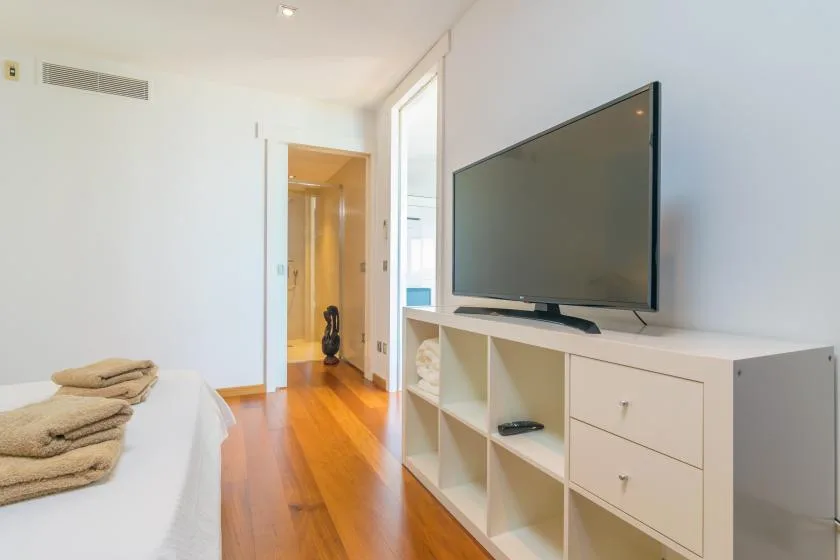 A bright bedroom with a bed beside a television and wooden flooring.