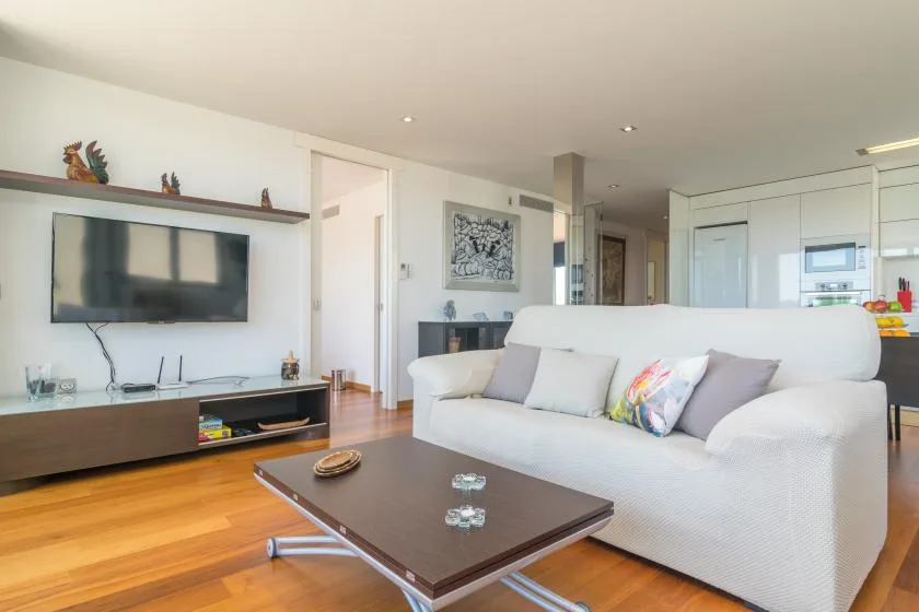 A bright living room with a white sofa, television, and coffee table.