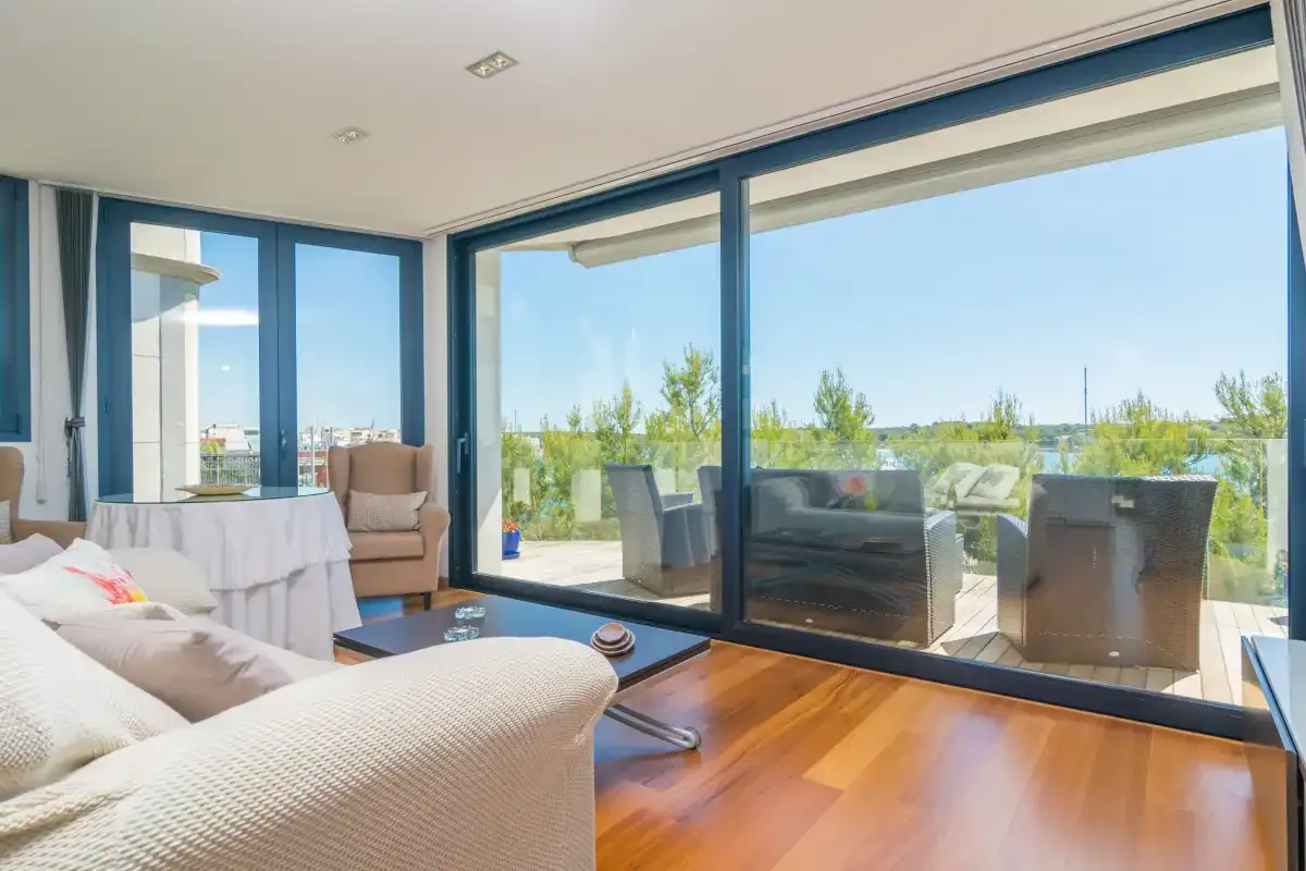 A bright living room opens onto a terrace through large glass doors.