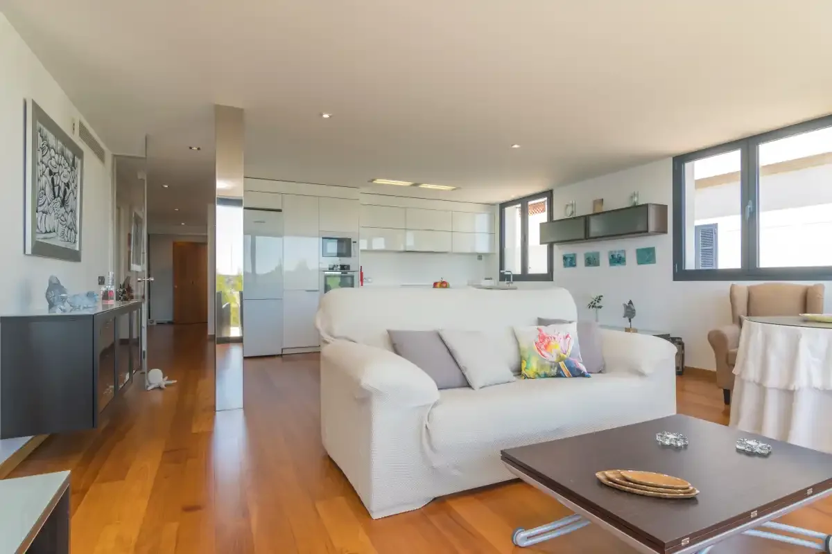 A bright living room with white seating and an open kitchen.