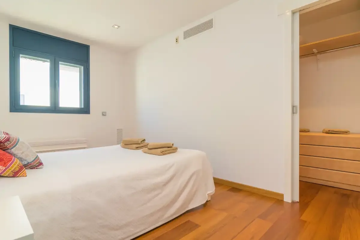 A bedroom with a bed, blue-framed windows, and wooden flooring.