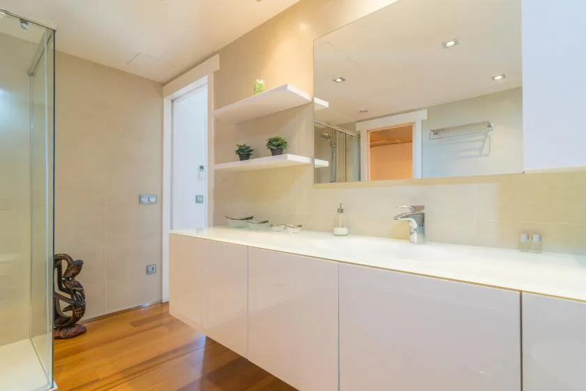 A bright bathroom with a long vanity, wide mirror, and glass shower.