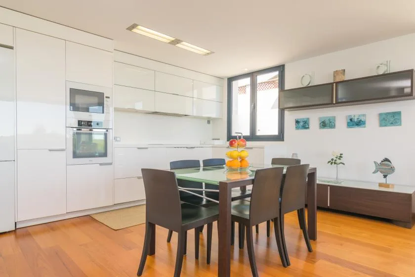 A bright dining area with a table and chairs beside a white kitchen.