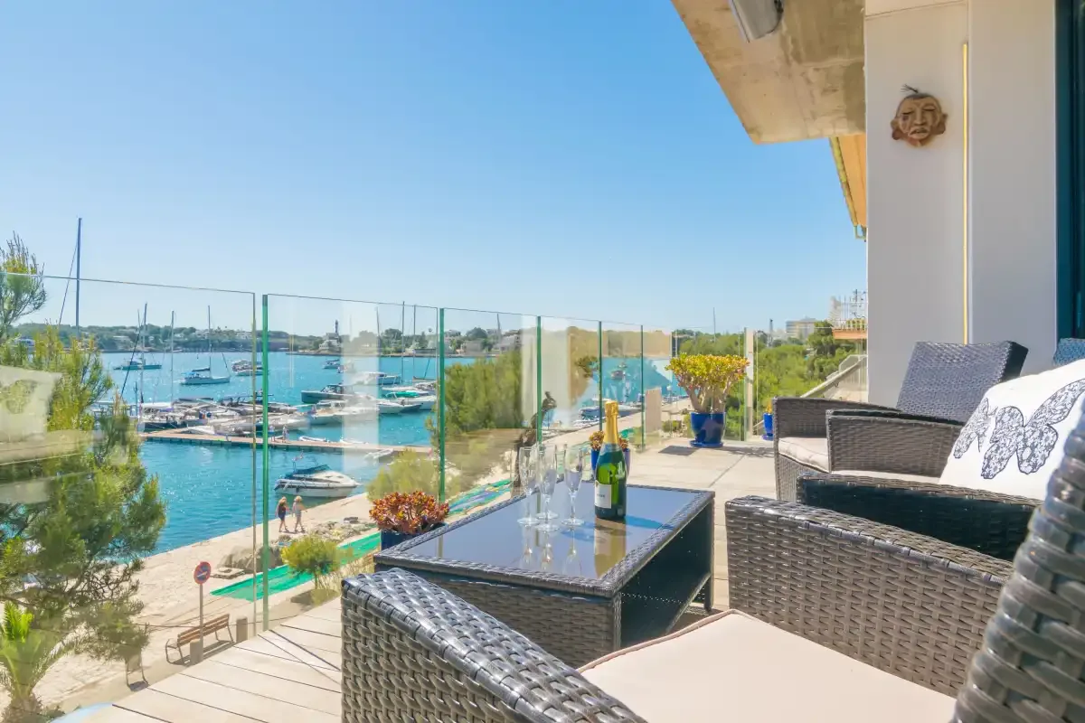 A waterfront terrace overlooks a marina, with outdoor seating and a glass railing.