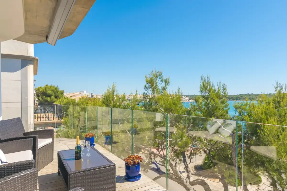 A balcony with outdoor seating overlooks trees and a distant shoreline.
