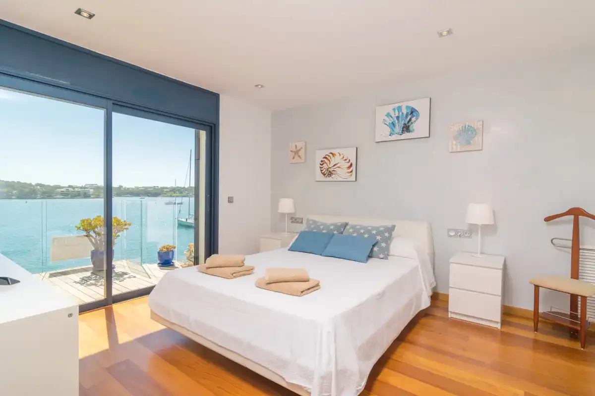 A bright bedroom with a large bed beside glass doors overlooking the water.