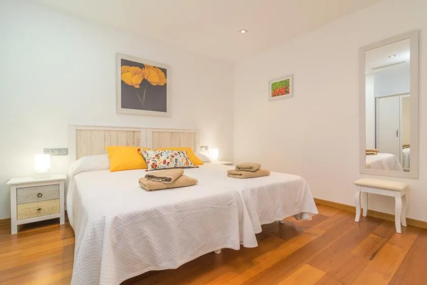 A bright bedroom with a neatly made bed and framed floral artwork.