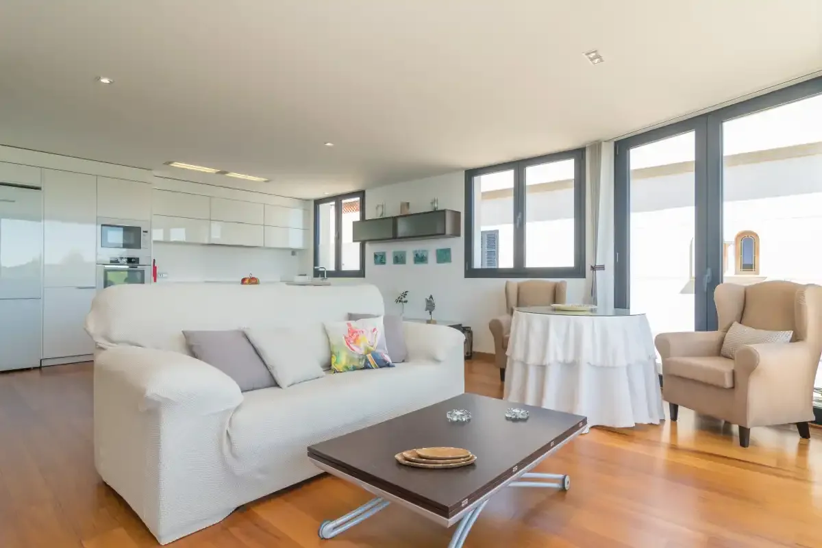 A bright living room with white seating, a coffee table, and an open kitchen.