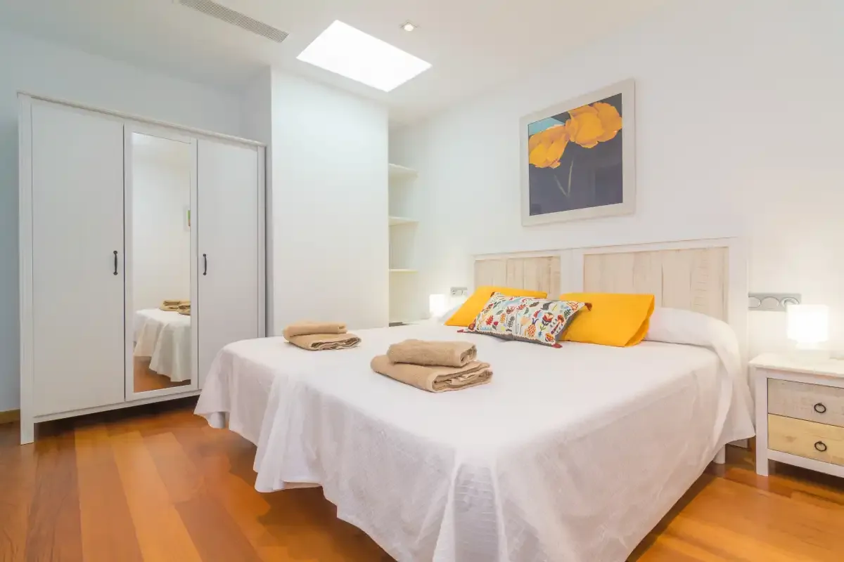 A bright bedroom with a neatly made bed and mirrored wardrobe.