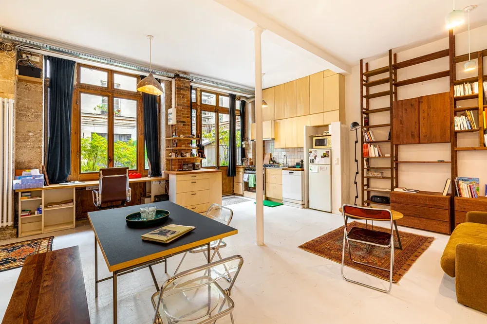 A bright open-plan living and kitchen area with large windows and built-in shelving.