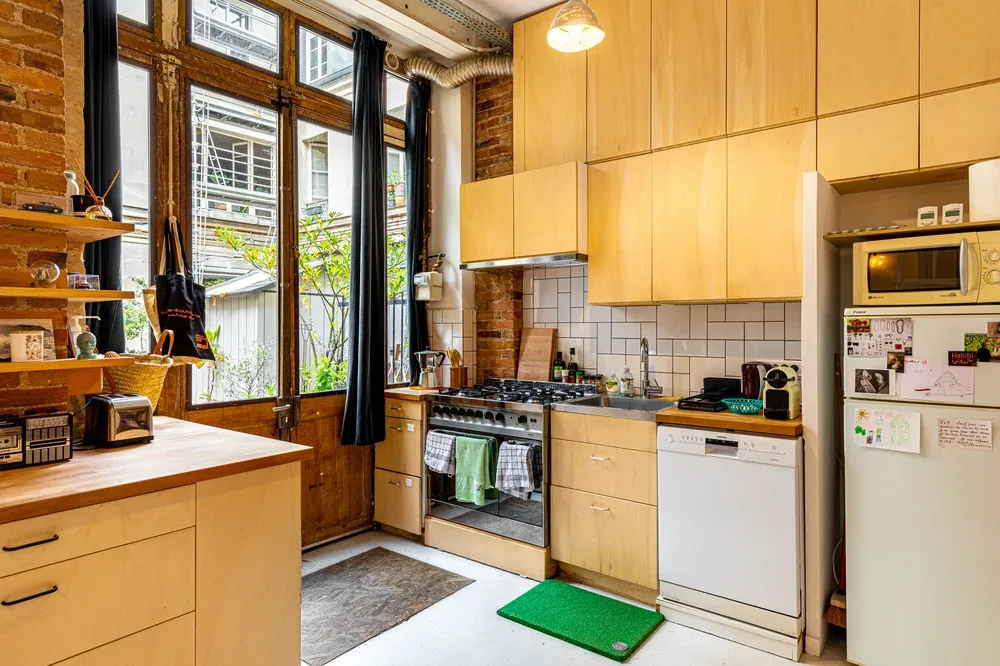 A kitchen with pale cabinetry, a stove, and tall windows.