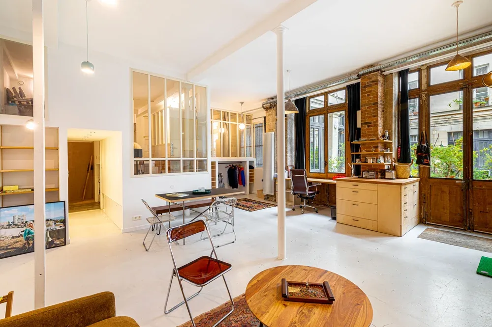 Un estudio diáfano y luminoso con una mesa de comedor y grandes ventanas.