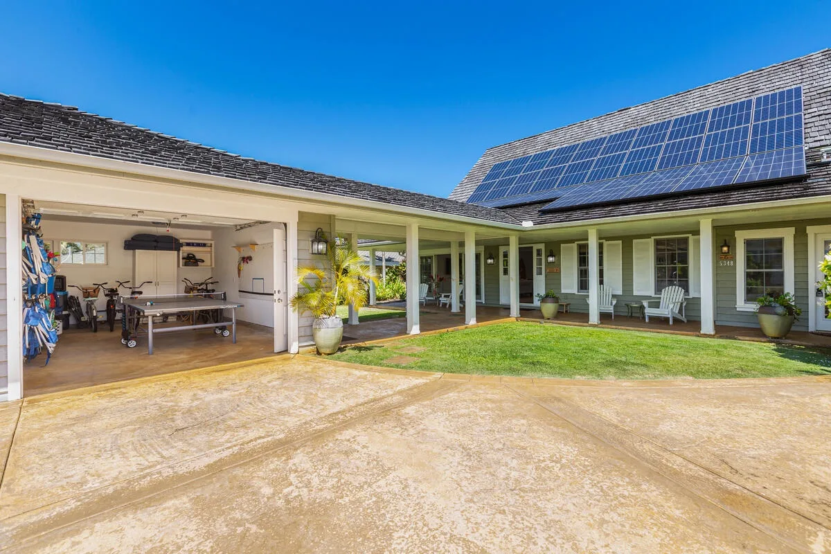 Una casa de una planta con patio pavimentado, césped y paneles solares en el techo.