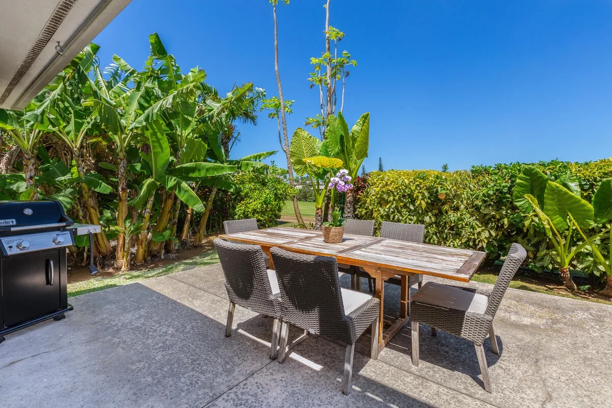 Una zona de comedor al aire libre con mesa de madera y sillas junto a plantas tropicales.