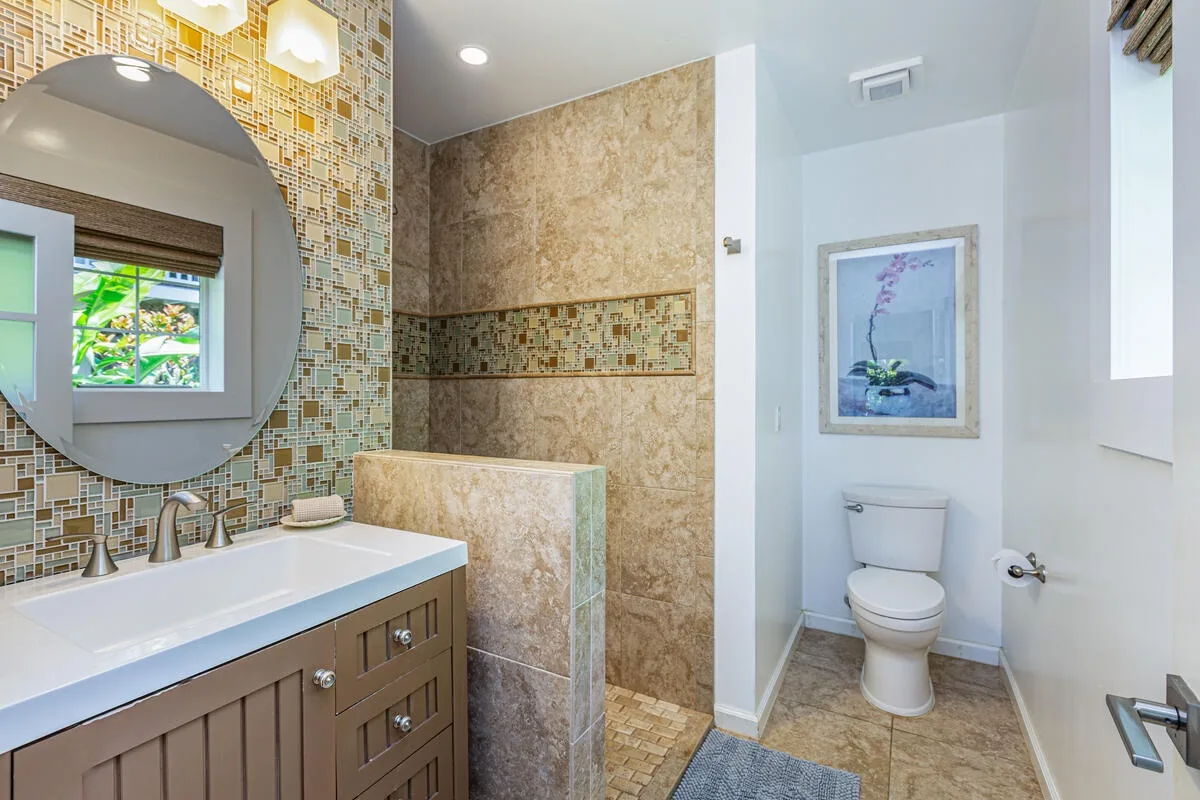 Un baño con tocador, espejo grande y área de ducha con azulejos.